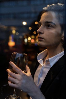 Pencerenin önünde şarap kadehi tutan genç bir kadın.