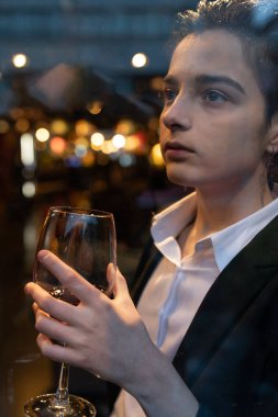 Pencerenin önünde şarap kadehi tutan genç bir kadın.