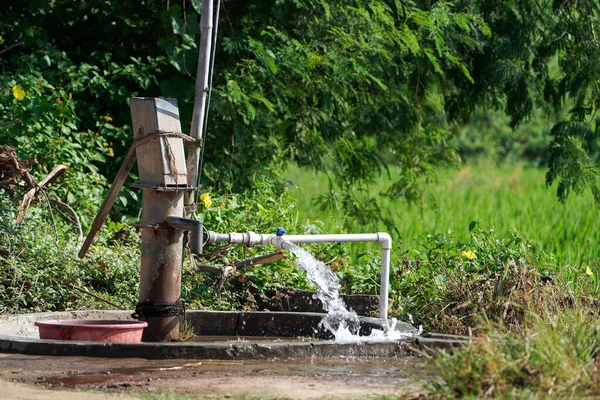 ポンプパイプからの水の流れと古い手は 畑の背景に農業用水ポンプのプラスチックパイプから噴出する農村部のインドの高圧水をポンピング水を運営し 背景に木や緑と青空 選択的焦点 — ストック写真