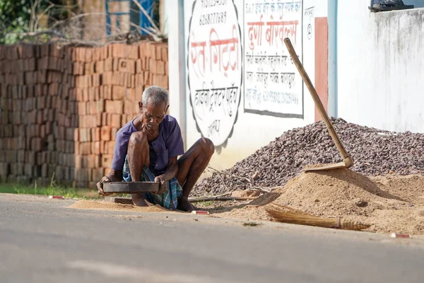 KACHANDA, CHHATTISGARH, İNDİYA, 15 Kasım 2022: Hindistan köyünde sabah yol kenarında oturan kumları filtreleyen yaşlı bir Hintli.
