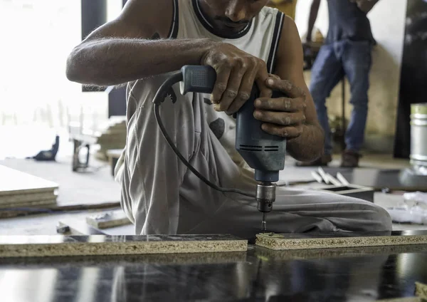 Marangozun atölyedeki matkapla ahşap delme makinesini, atölyedeki elektrikli matkabı kullanarak yakın plan işçilerinin ön görüşü. Ahşap mobilya üretiminde doğrama işi..