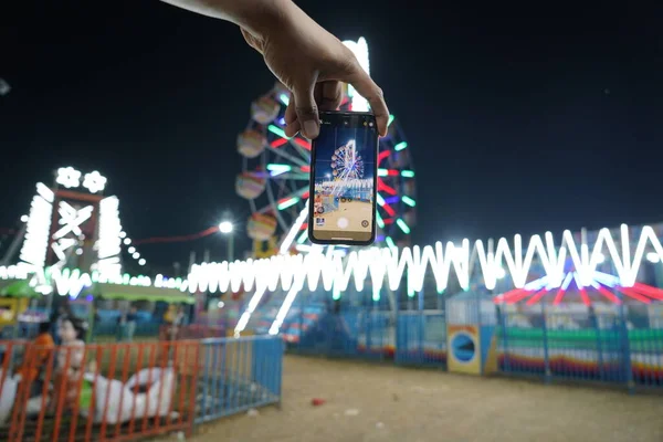男子手持手机夜间在印度集市上从智能手机上拍下巨型摩天轮的影像或照片 在手机或智能手机上拍出巨型摩天轮的影像 — 图库照片
