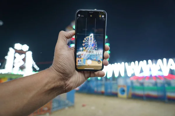 男子手持手机夜间在印度集市上从智能手机上拍下巨型摩天轮的影像或照片 在手机或智能手机上拍出巨型摩天轮的影像 — 图库照片