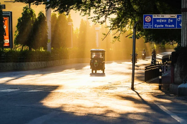 Beautiful yellow sun rays touching the empty road of raipur, an electrical auto rishaw passing in empty road at morning and sunlight crossing through trees, scenary, beauty of raipur, chhattisgarh