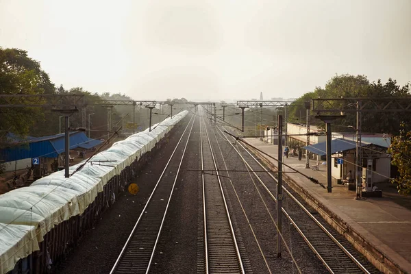 Hindistan 'da bir yük treni sol taraftaki tren istasyonunda duruyor ve boş tren raylarının görüntüsü, köprünün tepesinden bir fotoğraf.