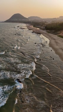 Sakin suları, kumlu sahili ve doğal tepe manzarası olan sahili, dağ arkası sakin sahili, yumuşak dalgaları ve altın saat ışığı olan sakin sahili, narin okyanus dalgaları ve arka planda tepeleri olan güzel bir sahil manzarası..