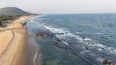 Sakin suları, kumlu sahili ve doğal tepe manzarası olan sahili, dağ arkası sakin sahili, yumuşak dalgaları ve altın saat ışığı olan sakin sahili, narin okyanus dalgaları ve arka planda tepeleri olan güzel bir sahil manzarası..