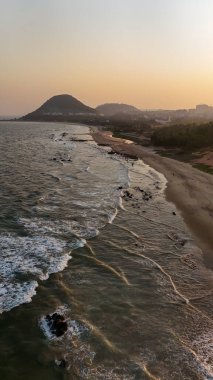 Sakin suları, kumlu sahili ve doğal tepe manzarası olan sahili, dağ arkası sakin sahili, yumuşak dalgaları ve altın saat ışığı olan sakin sahili, narin okyanus dalgaları ve arka planda tepeleri olan güzel bir sahil manzarası..