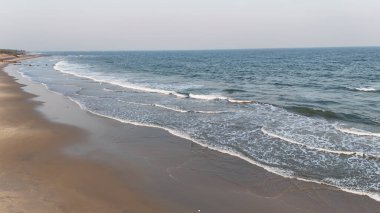 Berrak bir günde sakin okyanus dalgalarıyla geniş kumlu sahil, yumuşak sörf ve açık gökyüzü ile huzurlu sahil manzarası, yumuşak dalgalar ve temiz kumla doğal deniz manzarası, mavi sularla dolu sakin sahil manzarası ve boş kıyı şeridi, vizag konumu.