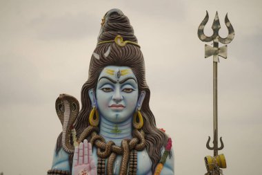 Lord Shiva 'nın mızraklı büyük heykeli, geleneksel elementleri olan kutsal Shiva heykeli. Bulutlu gökyüzünün altında Hindu tanrısı Shiva heykeli, tapınak alanında Shiva' nın huzurlu görüntüsü..