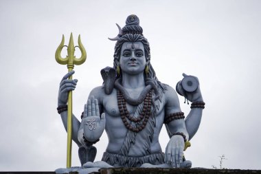 Lord Shiva 'nın mızraklı ve damarulu görkemli heykeli, Hindu tanrısı Shiva' nın kutsal tasviri kutsanmış poz, Trishul ve Damaru 'yu bulutlu gökyüzünün altında tutan büyük Shiva putu, Tanrı Shiva' nın ruhani heykeli, ilahi gücün sembolü..