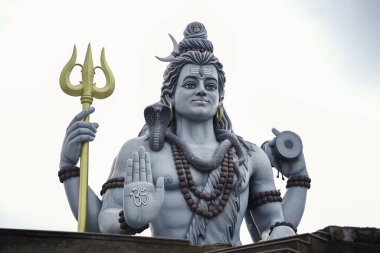 Lord Shiva 'nın mızraklı ve damarulu görkemli heykeli, Hindu tanrısı Shiva' nın kutsal tasviri kutsanmış poz, Trishul ve Damaru 'yu bulutlu gökyüzünün altında tutan büyük Shiva putu, Tanrı Shiva' nın ruhani heykeli, ilahi gücün sembolü..