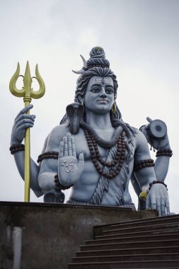 Lord Shiva 'nın mızraklı ve damarulu görkemli heykeli, Hindu tanrısı Shiva' nın kutsal tasviri kutsanmış poz, Trishul ve Damaru 'yu bulutlu gökyüzünün altında tutan büyük Shiva putu, Tanrı Shiva' nın ruhani heykeli, ilahi gücün sembolü..