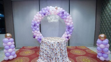 Doğum günü veya bebek etkinliği dekorasyonu, Balon kemeri parti arka planı, kapalı bebek partisi sahnesi, balon temalı kutlama salonu, mor ve pembe balon dekoru, bebek partisi dekorasyonu.