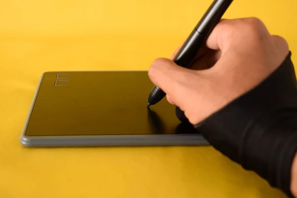 The hand wearing glove draws on a graphics tablet. Freelance, designer, Illustrator on yellow background