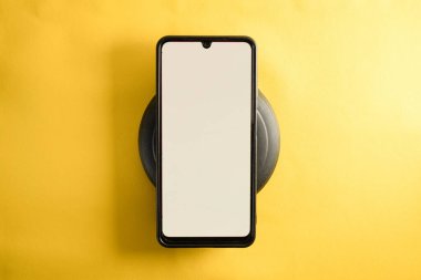Beyaz ekranlı akıllı telefonun üst görüntüsü ve sarı arkaplanda izole edilmiş telefon veya mini tripodun parçaları