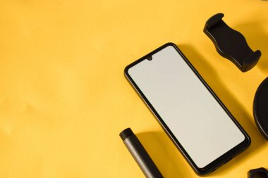Beyaz ekranlı akıllı telefonun üst görüntüsü ve sarı arkaplanda izole edilmiş telefon veya mini tripodun parçaları