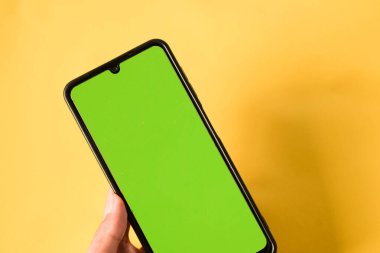 el ele tutuşan modern cep telefonu yeşil ekran sarı arka planda izole