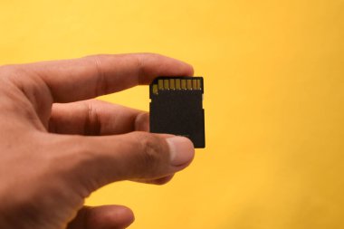 DSLR ya da sarı arkaplanda aynasız kamera için SD kart tutuyor