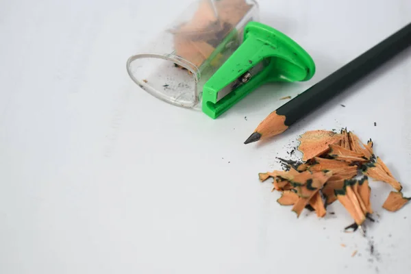 green pencil sharpener and dark green pencils, pencil shavings on white background