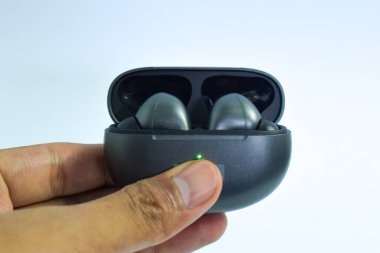 El ele tutuşan TWS veya kablosuz kulaklık beyaz arka planda izole edilmiş, True Wireless Stereo, buds, şarj oluyor.