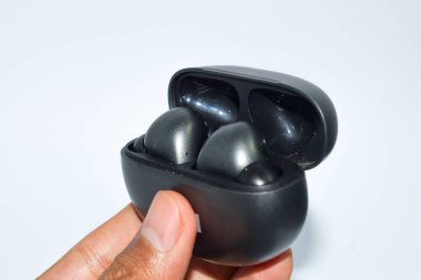 El ele tutuşan TWS veya kablosuz kulaklık beyaz arka planda izole edilmiş, True Wireless Stereo, buds, şarj oluyor.