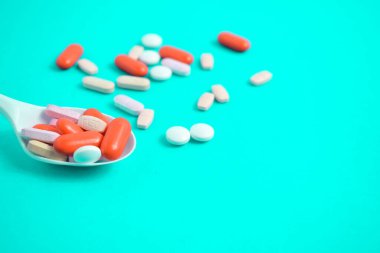 Yeşil Tosca arka planında beyaz kaşıkta renkli ilaç hapları, takviye, vitamin, renkli