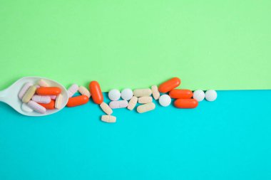 Yatay yeşil ve mavi arka planda renkli ilaç içeren beyaz kaşık.