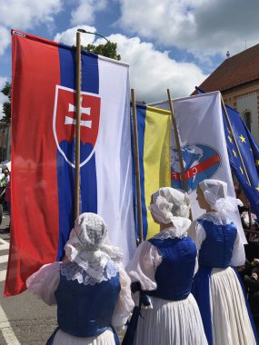 Myjava, Slovakya, 17 Haziran 2023: Uluslararası Folklor Festivali vesilesiyle kostüm giymiş kadınlar bayrak taşıyor. Şehrin içinden geçen bir geçit töreninin parçaları..
