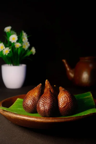 A typical tropical fruit called snake fruit ,on the table with tea pot and flowers.