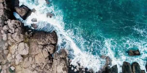 青い海の岩の上からの波の空中トップビュー 美しいビーチの空中ビュードローン4Kショットで海の波 空の石の崖の上から海の波の鳥の目のビュー — ストック動画