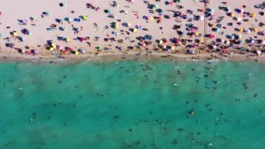 Renkli şemsiyeler, yüzen ve güneşlenen insanlar, İzmir Cesme bölgesinin ünlü Ilica plajında güneşlenen şezlonglar ve dalgalar. Yüksek kalite 4k görüntü