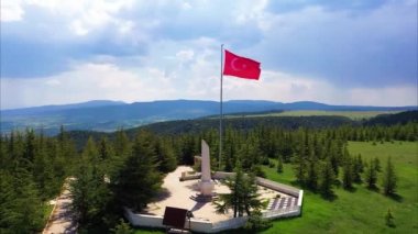 Ormandaki mezarlığın üzerinde bulutlu bir gökyüzünde dalgalanan Türk bayrağının hava görüntüsü. Yüksek kaliteli FullHD görüntüler