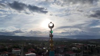 Bulutlu bir günde cami minaresinde İslam 'ı temsil eden hilal görüntüsü ve arkasında güneş parlıyor. Yüksek kalite 4k görüntü