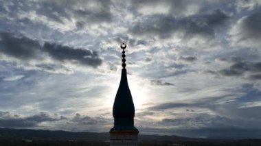 Bulutlu bir günde cami minaresinde İslam 'ı temsil eden hilal görüntüsü ve arkasında güneş parlıyor. Yüksek kalite 4k görüntü