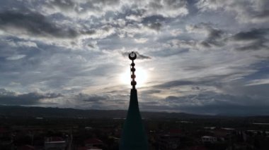 Bulutlu bir günde cami minaresinde İslam 'ı temsil eden hilal görüntüsü ve arkasında güneş parlıyor. Yüksek kalite 4k görüntü