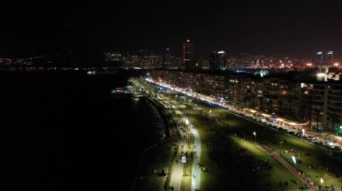 İzmir şehrinin gece manzarası, deniz kenarındaki binalar ve sahildeki insanlar. İzmir 'deki gezinti güvertesi boyunca İHA atışı. Yüksek kalite 4k görüntü