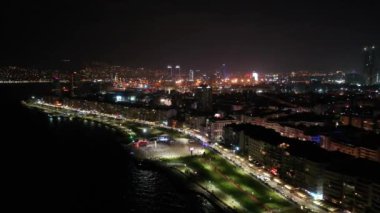 İzmir şehrinin gece manzarası, deniz kenarındaki binalar ve sahildeki insanlar. İzmir 'deki gezinti güvertesi boyunca İHA atışı. Yüksek kalite 4k görüntü