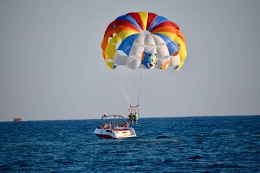 Mavi gökyüzünde bir tekne tarafından çekilen iki kişi. Çok renkli deniz paraşütü. Tekneyle karaya çıkıyor.. 