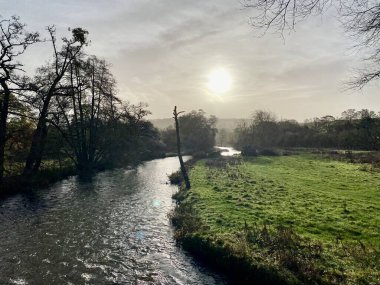 River Wye, Derbyshire, İngiltere. Güneşin bulutlarda yandığı kış sahneleri.. 