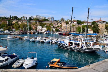Türkiye 'nin Antalya Limanı' nda demirli tekneler, Kasım 2022. Mavi gökyüzü, su ve arkadaki binalar. Taş şehir duvarları arkasında. Mavi gökyüzü.