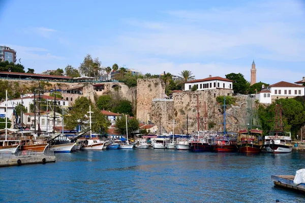 Türkiye 'nin Antalya Limanı' nda demirli tekneler, Kasım 2022. Mavi gökyüzü, su ve arkadaki binalar. Taş şehir duvarları ve minare. 
