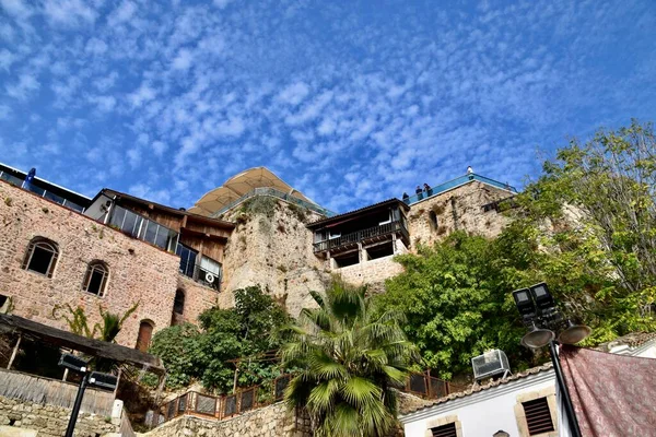 View upwards of stone houses with deep blue sky and cirrocumulus clouds. Green plants in between.