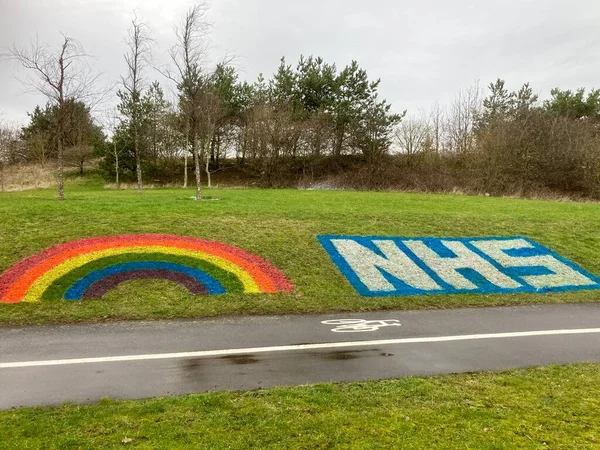 NHS Logo with Rainbow painted on grass bank.Derby, England, UK. February 20, 2021. 
