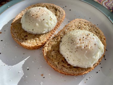 Poached eggs on brown toast with salt and pepper. Sunlight casting a shadow. 