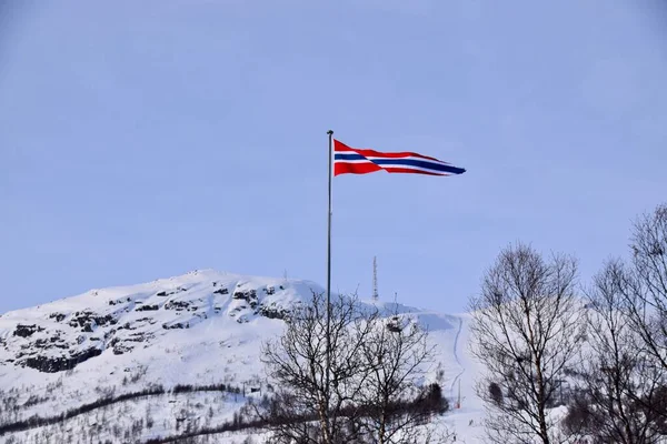 Norwegian Flag flying over ski slopes. Ski run behind. Hovden, Norway, Feb 2023.
