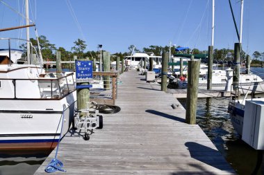 Gemiler ahşap bir iskeleye demirlemiş, arkasında ağaçlar, mavi gökyüzü. Manteo, ABD, 1 Ekim 2019. 