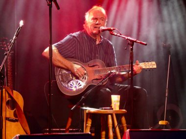 Ralph McTell, The 2019 Cambridge Halk Festivali 'nde canlı performans sergiliyor. Şarkı söyleyerek ve gitar çalarak.