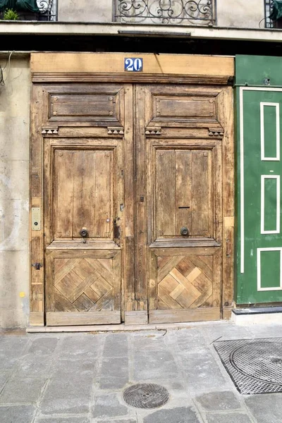 Rustic Brown wooden door with number 20 over. Green wall to the right. Paris France. March, 2023.