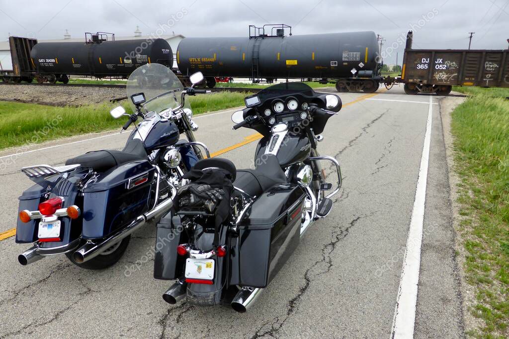 2 Black Harley Davidson Motorcycles waiting at a crossing for a freight train to pass.Illinois, USA. June 4, 2014.